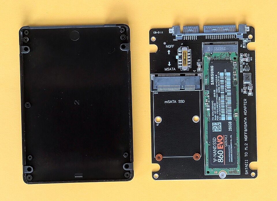 Dysk SSD w adapterze obok otwartej obudowy laptopa